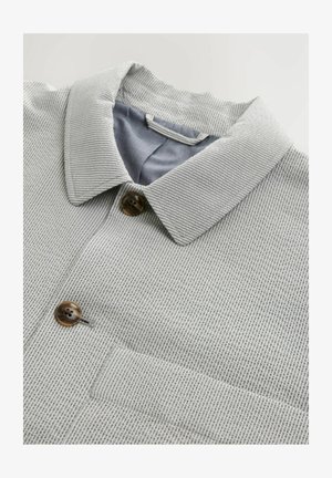 Harmaa kuvioitu paita, jossa on kauluspantalon kaulus, kaksi ruskeaa nappia ja sininen sisävuori. Rakennepinta, jossa on vaakasuorat raidat.