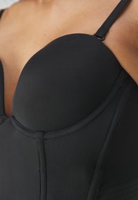 Svart strukturert bodysuit med glatt stoff og undertråkkopper. Har justerbare stropper og sydd detaljer langs sømmene.