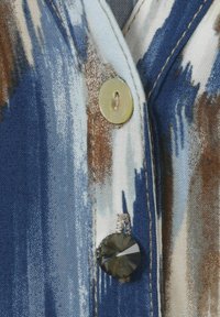 Geknöpftes Stoffelement in Blau-, Braun- und Weißmustern; umfasst einen runden, facettierten Kristallakzent und einen beigen Knopf.