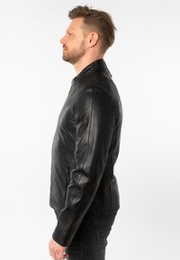 Giacca in pelle nera con un design aderente, colletto alto e tasca laterale con zip. Presenta una texture liscia e dettagli di cucitura sottili.