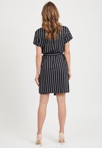 Vestido de rayas negras con mangas cortas, cintura ceñida y falda hasta la rodilla. Llevado con zapatos de tacón claros.