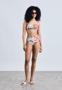 Daudzkrāsains bikini ar ziedu rakstu; krūštura tipa augšdaļa ar regulējamām lencītēm un augsta vidukļa apakšdaļa ar sānu saitēm. Modelis valkā tumšas saulesbrilles.