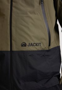 Giacca verde oliva e nera realizzata in tessuto texturizzato, presenta una zip frontale, dettagli con logo e un design a blocchi di colore.