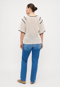 Knit beige top with short, puffed sleeves and black trim, paired with light blue jeans. Texture is open-weave, casual design.