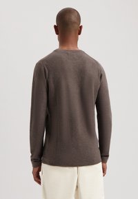 Pulover din lână texturat, de culoare maronie, cu mâneci lungi și gât rotund, având un tiv și mansete cu model elastic, prezentat din spate.