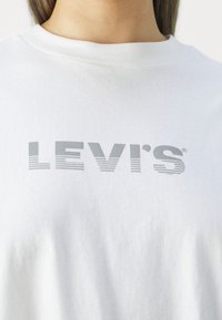 Camiseta de algodón blanca con el logo "LEVI'S" en gris y un diseño de degradado. Cuello redondo clásico y textura suave.