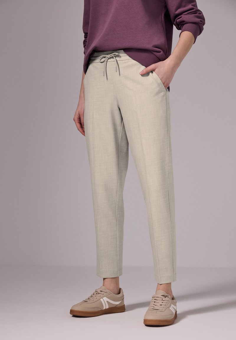 Lichtgrijze op maat gemaakte broek met een gestructureerde afwerking, elastische tailleband, zijzakken, gecombineerd met beige sneakers met witte accenten.