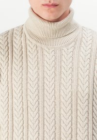 Maglione a collo alto in crema con motivi a trecce in rilievo, dotato di un colletto a coste e un tessuto strutturato, realizzato in filato morbido.