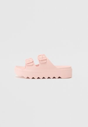 Lyserøde platformsandaler med to justerbare spænder, lavet af et glat materiale. Har en zigzag sål for ekstra greb og tekstur.