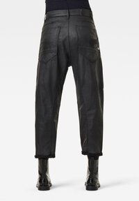 Černé kožené kalhoty volného střihu, které mají dvě zadní kapsy a ohrnuté nohavice. Hladká textura s viditelnými švy.