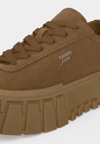 Baskets marron épaisses avec semelle épaisse et lacets texturés, avec un petit logo argenté "tommy jeans" sur le côté.