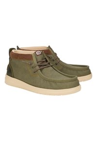 Zapatillas de lona verdes con un cuello de pana color marrón, suela de goma y cordones marrones. Presenta costuras sutiles y un logo en la lengüeta.