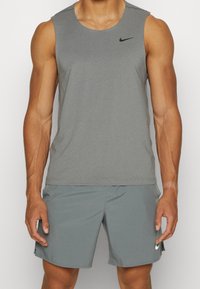 Graues ärmelloses Sportoberteil mit rundem Halsausschnitt, mit dem Nike-Logo in Schwarz, kombiniert mit passenden grauen Shorts und Stofftextur.