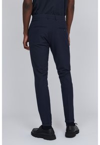 Navy blue trousers with a fitted design, cotton blend material, two back pockets, and cuffs rolled above ankle, paired with black shoes.