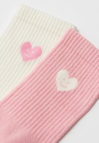 Twee paar geribbelde sokken; een paar in crème met een roze hartmotief, het andere paar in roze met een wit hartmotief. Zacht van textuur.