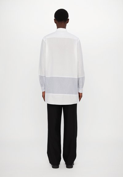 Chemise blanche à manches longues avec un panneau arrière en-rayures verticales bleues et blanches. Présente un col classique et une coupe décontractée.