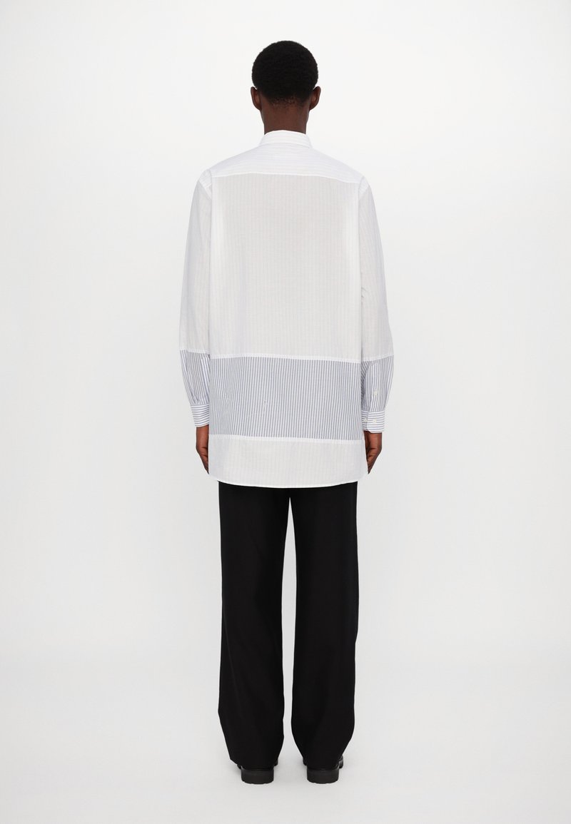 White long-sleeve shirt with a back panel of vertical blue and white stripes. Features a classic collar and relaxed fit.