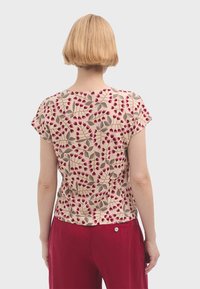 Blusa a maniche corte con motivo floreale in rosso e verde su sfondo beige, con una vestibilità rilassata e una trama di tessuto morbido.