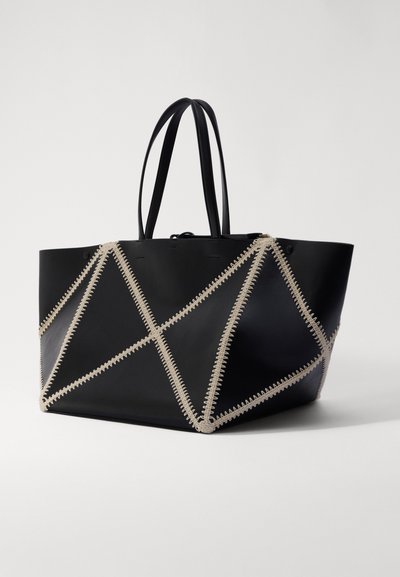 Black tote bag made of smooth leather, featuring contrasting beige stitching in a geometric pattern, with two sturdy handles.