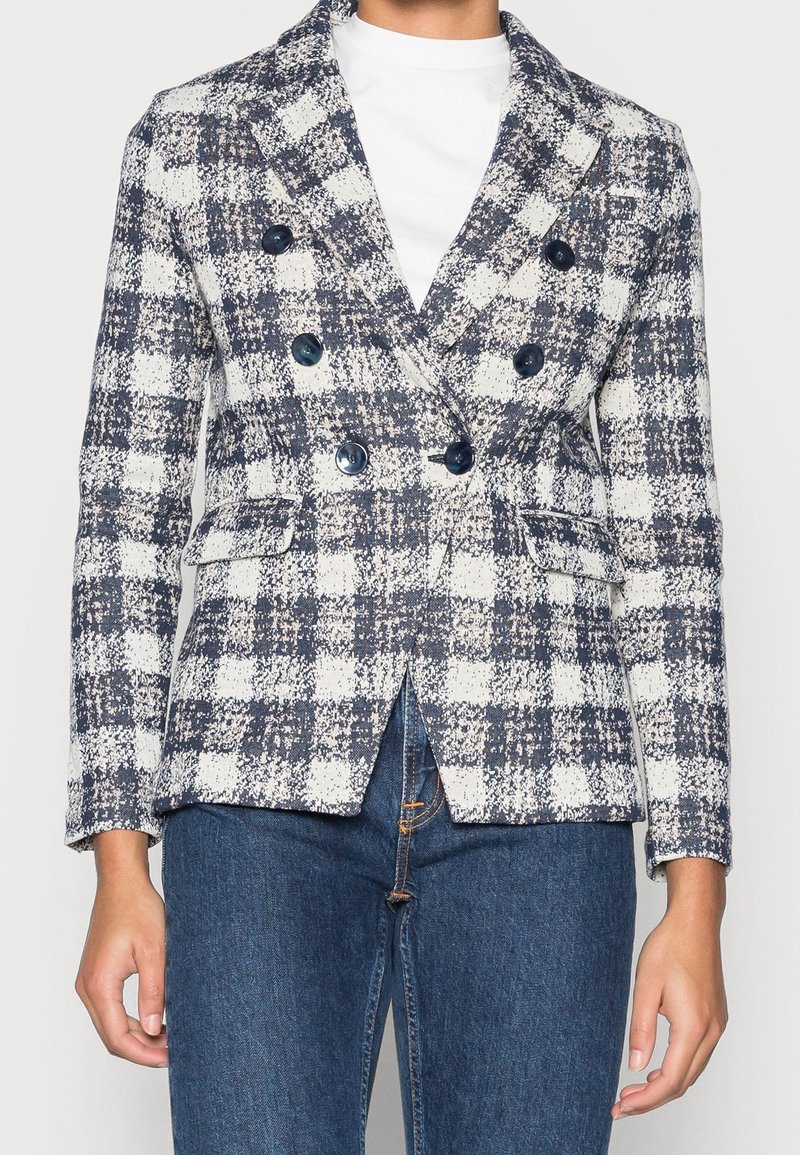 Blazer de doble botonadura en un patrón de cuadros azul marino y blanco, con botones grandes, un corte entallado y dos bolsillos delanteros.
