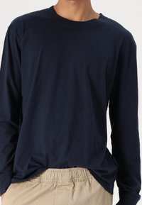 Navy long-sleeve shirt in soft cotton with a round neckline and relaxed fit. Features subtle branding on the chest and smooth texture.