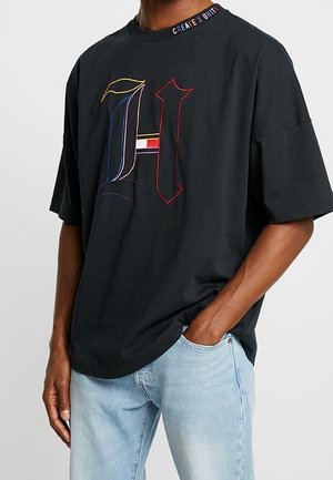 Czarna koszulka z oversize'owym krojem, z wielokolorowym haftowanym "H" z przodu oraz napisem "CREATE UNITY" na kołnierzyku. Wykonana z miękkiej bawełny.