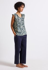 Top senza maniche elegante in una stampa serpente verde e blu, abbinato a pantaloni larghi blu navy. Il top presenta un delicato dettaglio arricciato sulla spalla.