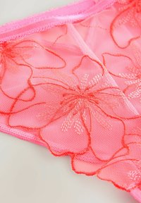 Pink lace panties featuring floral embroidery in orange thread, showcasing a sheer mesh texture and scalloped edges.