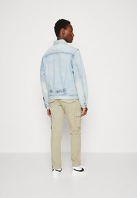 Chaqueta de mezclilla azul claro con un corte clásico y detalles de costura visibles, combinada con pantalones cargo beiges que cuentan con bolsillos laterales.