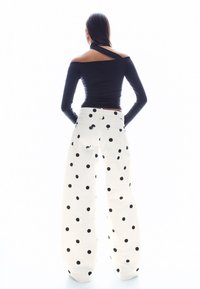 Fekete hosszú ujjú felső nyitott hátrésszel és fehér, fekete nagy pöttyökkel díszített, bő szárú nadrággal. Az outfit hátulról látható.