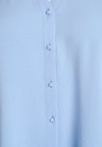 Light blue fabric with a vertical row of matching covered buttons and visible stitching along the button placket.