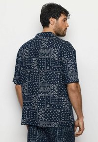 Námořnická košile s krátkým rukávem zdobená bílým paisley vzorem a geometrickými akcenty. Vyrobena z lehkého materiálu s volným střihem a límečkem.