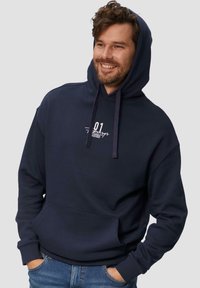 Navyblauwe hoodie met een voorkantzak, trekkoorden en een gedrukt ontwerp op de borst. Heeft een ontspannen pasvorm en een zachte stoftextuur.