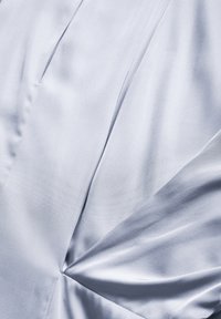 Vaaleansininen satiinikangas, jossa on sileä rakenne, johon on käytetty vinoja poimintoja ja keskeistä rypytystä, luoden visuaalista syvyyttä ja kiinnostavuutta.