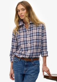 Geruite flanellen overhemd in blauw, rood en wit met een button-down kraag. G gedragen met lichtblauwe jeans en een bruine gevlochten riem.