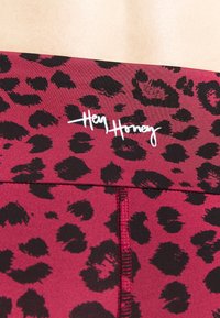 Legíny s leopardím potiskem v burgundské a černé barvě, s bílým logem "Hey Honey" na pase. Hladký materiál s jemným žebrováním.