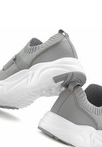 Graue Sportschuhe mit einem strukturierten Strick-Obermaterial und glatten, synthetischen Einsätzen, einer klobigen weißen Sohle und einer Zuglasche an der Ferse.