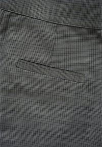 Tela de cuadros gris con una sutil textura, que presenta un bolsillo de welt plano integrado de manera fluida en el diseño.