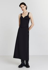 Schwarzes Zweiteiler-Outfit mit einem taillierten, strukturierten Oberteil mit breiten Trägern und einem langen, fließenden Rock mit silbernen Hardware-Akzenten.