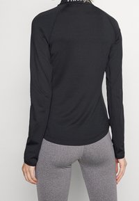 Černý sportovní top s dlouhým rukávem vyrobený z hladkého materiálu, s kulatým lemem a jemným logem na límci.