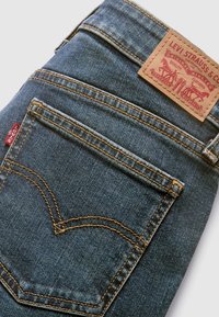 Jean en denim bleu plié, montrant la poche arrière avec une couture orange et un patch de marque en cuir Levi Strauss & Co.