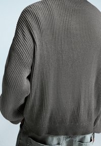 Pull tricoté gris foncé avec texture côtelée, design court et manches amples. Dispose d'un col large et d'une coupe décontractée.