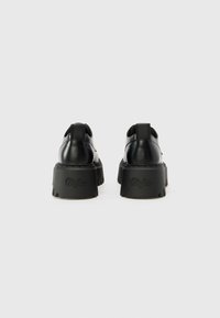 Black platform shoes with a smooth leather finish, round toe, and deeply ridged rubber outsole. Features embossed logo on the heel.