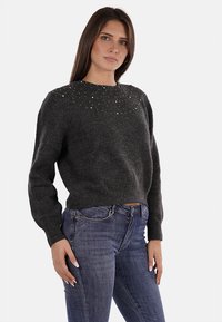 Maglione corto grigio scuro con scollatura arrotondata, caratterizzato da decorazioni in perline lungo la parte superiore del corpo. Texture morbida e polsini a coste.