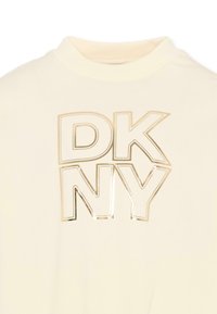 T-shirt color crema con collo alto e grande logo "DKNY" in oro metallizzato a caratteri cubitali. Tessuto liscio e design minimale.
