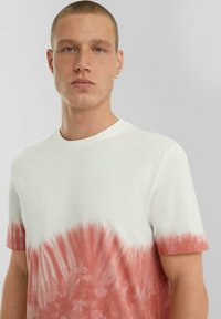 Wit T-shirt met korte mouwen met een rood tie-dye patroon, voorzien van een ronde hals en een zachte katoenen textuur. Geen zichtbare logo's of versieringen.