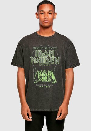 Svart överdimensionerad t-shirt i bomull, med ett grönt grafiskt tryck som inkluderar text och en illustration relaterad till Iron Maidens turné 1985.