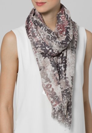 Femme portant un haut blanc sans manches et une écharpe ample avec des motifs abstraits aux tons rouge atténué, gris et noir.