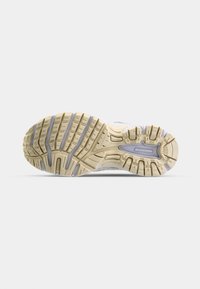 Semelle de chaussure de sport avec une surface en caoutchouc texturée ; présente des motifs de semelle proéminents et une couleur beige clair avec des accents gris.