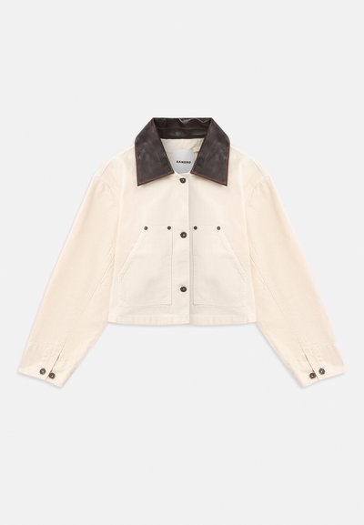 Jachetă scurtă bej cu guler din piele maro închis, închidere cu nasturi în față, două buzunare la piept și manșete cu nasturi.